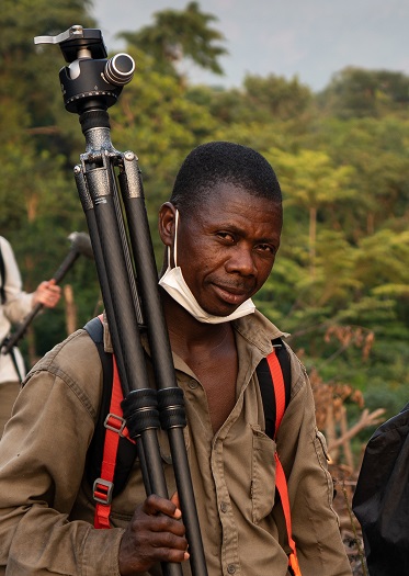 Field assistant Cé Vincent Mami photpgraphed carrying a tripod in Bossou during filming of the documentary featuring chimps of Bossou, taken by Kalyanee Mam