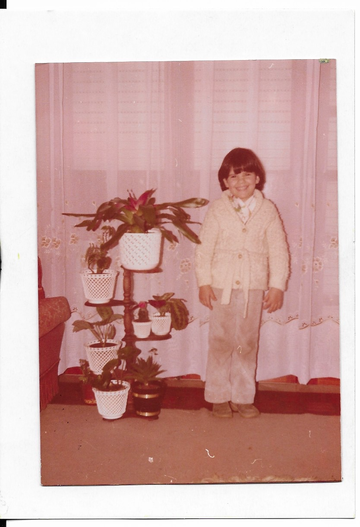 Susana photographed in 1981, aged 8 years old, smiling beside a number of house plants.